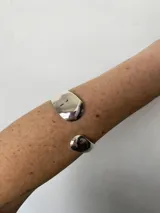 Brazalete plateado abierto, con forma irregular y terminaciones redondeadas.