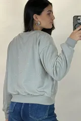 Buzo de cuello redondo y manga larga, color negro, con diseño de pequeños puntos brillantes distribuidos por toda la prenda. Presenta puños y ruedo acanalados.