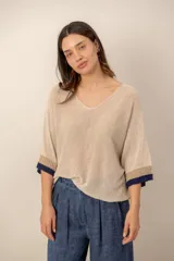 Sweater de punto beige, con escote en V holgado, mangas tres cuartos y detalles de ribetes en tono marrón y azul marino en los puños.