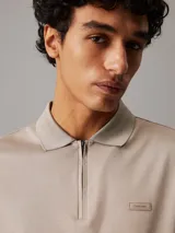 Chomba Calvin Klein color beige con cuello polo y media cremallera. Tiene mangas cortas y un parche de goma con el logo de la marca.