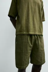 Bermuda de algodón color verde oliva, con corte relajado y textura acanalada vertical. Presenta cintura elástica con cordón interior y bolsillos laterales y trasero.