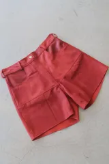 Bermuda de cuero napa color rojo, de tiro alto con trabillas para cinto, bolsillos delanteros redondeados y costuras decorativas.