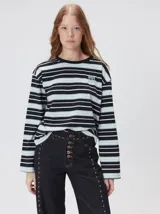 Remera de manga larga con diseño a rayas horizontales en tonos azul, blanco y negro. Presenta un cuello redondo al tono y un logo bordado en el pecho. El diseño destaca por tener un patrón de rayas diferente en las mangas y un calce holgado.