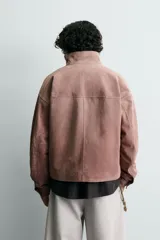 Cazadora de corte cropped confeccionada en piel con acabado serraje. Presenta cuello subido, cierre frontal de cremallera, manga larga con puños abotonados y bolsillos laterales de vivo.