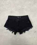 Short de denim negro de tiro medio, con bolsillos delanteros y traseros, pasatintos y dobladillo desmechado con flecos.