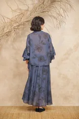 Conjunto de dos piezas compuesto por una camisa de manga larga con volados frontales y cierre de botones, y una falda larga a juego. Ambas prendas presentan un estampado floral en tonos azulados.