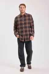 Camisa de manga larga con cuello camisero y botones frontales, confeccionada en tejido de franela con patrón de cuadros escoceses en tonos marrón oscuro, negro y beige.