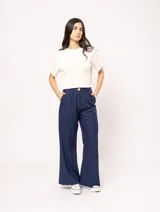 Pantalón de lino color beige, de tiro alto, pierna ancha y levemente acampanada. Tiene pinzas delanteras, elástico en la pretina trasera, cierre delantero y broche interno, bolsillos laterales y dobladillo invisible.