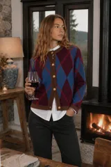 Cardigan de punto con patrón argyle en tonos azul y bordó, con bordes en color marrón, cuello redondo y cierre frontal con botones dorados.
