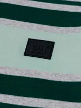 Remera polo gris melange de manga corta Caterpillar, con franjas horizontales en tonos verde oscuro y menta en el pecho, cuello camisero con botones y parche de silicona con logo.