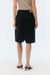 Bermuda oversize de denim color negro, con diseño de cinco bolsillos, cierre de botón y ojal, y ruedo deshilachado.