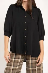 Blusa de corte oversize en color blanco, con cuello camisero, cierre frontal de botones y mangas tres cuartos con sutiles frunces en los hombros.