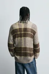 Jersey de punto con estructura abierta y calce relajado. Presenta cuello redondo, manga larga y diseño a rayas horizontales en tonos marrón y gris con detalles en amarillo neón. Acabados en rib en puños y ruedo.