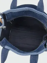 Cartera tipo tote bag de Marc Jacobs, confeccionada en denim con diseño de patchwork en diferentes tonos de azul. Presenta el logo estampado en el frente, doble asa superior y correa de hombro ajustable y extraíble en color azul marino con detalles en cuero tostado.