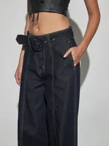 Jean azul oscuro de corte wide leg y tiro alto, con costuras pespunteadas verticales al frente y cinturón incorporado con hebilla cuadrada.