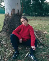 Buzo unisex de tejido de punto grueso en lana merino, color rojo, con cuello redondo y diseño de calce relajado. Presenta un detalle bordado a mano en contraste en la manga.