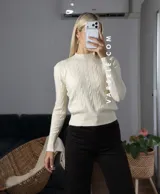 Sweater de tejido de punto con diseño de trenzas verticales, cuello redondo y mangas largas con puños ajustados que presentan detalle de botones metálicos.