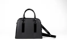 Cartera tipo bowling de cuero vacuno color negro, con doble asa corta y correa larga extraíble. Tiene cierre metálico YKK, bolsillo interno con cierre y logo de la marca grabado en el frente.