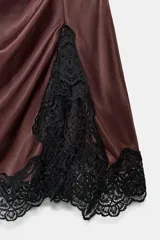 Vestido corto de cuello subido y sin mangas, confeccionado en tejido satinado. Presenta un detalle de fruncido lateral con abertura frontal y aplicación de encaje en el bajo.
