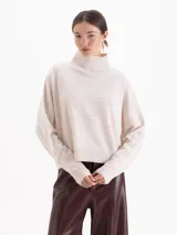 Polera de tejido de punto en color beige, con cuello alto, corte holgado y mangas largas con puños acanalados.