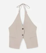 Chaleco color beige con escote halter, corte al cuerpo y cierre frontal con botones. Presenta un bolsillo de ojal en el frente.