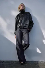 Chaqueta de Zara Woman Collection en tejido con acabado brillante efecto cuero. Presenta cuello solapa, manga larga con trabillas ajustables, bolsillos delanteros y cierre frontal con botones ocultos bajo solapa.