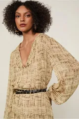 Vestido largo con estampado abstracto en tonos beige y marrón, de mangas largas con puños elásticos, escote en V con volantes y falda evasé con recortes. Incluye cinturón fino negro.