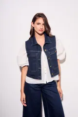 Chaleco de jean azul oscuro con cuello, bolsillos frontales y cierre con botones dorados. Corte al cuerpo.