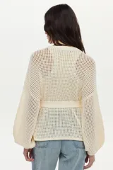 Sweater tejido en estructura calada, de color crudo, con mangas anchas, bordados decorativos en el frente y cinturón tejido incorporado.