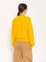 Sweater color marrón claro de tejido cerrado, con cuello redondo, mangas largas y largo a la primera cadera. Tiene un pequeño bordado rojo en el puño de la manga derecha.