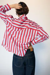 Camisa de manga larga con cuello subido y detalle de lazada frontal. Presenta un diseño de rayas verticales en tonos verde y celeste, con cierre frontal de botones y puños clásicos.