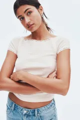 Top ajustado de manga corta con escote amplio que deja los hombros descubiertos, ribeteado con encaje blanco. El tejido es de punto de algodón con rayas finas verticales en tonos rosado pálido y blanco.