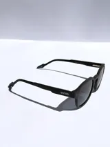 Lentes de sol con armazón de marco completo en color gris mate, con detalles decorativos en color rojo en las esquinas y patillas. Cuentan con cristales oscuros polarizados con protección UV 400.