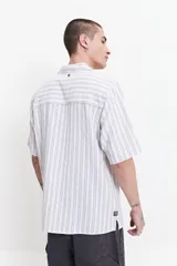 Camisa de manga corta a rayas verticales blancas y grises, con cuello camisero y corte recto. El modelo usa talle M.