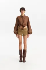 Camisa de manga larga abullonada, color marrón con estampado animal print sutil, cuello camisero y cierre frontal de botones. La parte inferior se anuda al frente dejando ver parte del abdomen.