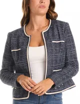 Chaqueta de tejido tweed en tono azul con sutiles destellos de lúrex. Presenta cuello a la base, abertura frontal y bolsillos decorativos. Las mangas largas incluyen detalle de botones metálicos dorados en los puños, y cuenta con vivos a contratono en los bordes.