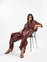 Camisa marrón con estampado de cadenas y flores rosadas, confeccionada en lino italiano. Tiene cuello clásico, silueta fluida y botón de flor en el cuello.