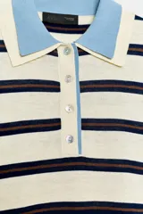 Jersey de punto con diseño a rayas horizontales en tonos crema, azul marino y marrón. Presenta cuello tipo polo en color celeste, cierre frontal con botones y puños y ruedo en tono celeste a juego.