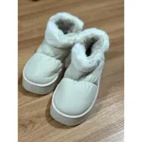 Pantuflas botitas color tostado con diseño acolchado y plataforma, forradas con corderito sintético blanco en el interior y el cuello. Cuentan con una pequeña etiqueta decorativa en el lateral.