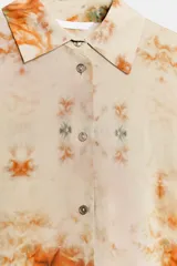 Camisa de manga larga con cuello solapa y cierre frontal con botones, con diseño tie-dye en tonos beige, naranja y verde oscuro en el sector inferior.