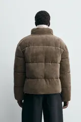 Cazadora acolchada de corte relajado confeccionada en tejido de pana. Presenta cuello subido, cierre frontal con cremallera, bolsillos laterales de vivo y bajo ajustable con elásticos laterales.