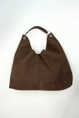 Bolso tipo hobo confeccionado en gamuza marrón, con diseño slouchy, asa corta de cuero y argollas metálicas plateadas.