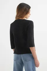 Cardigan verde esmeralda de tejido de punto calado, con mangas 3/4 y corte evasé. Presenta cuello redondo con abertura en forma de gota y cierre con un único botón.