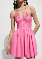 Vestido corto de color rosado con diseño evasé, escote halter con cuello fruncido y tirantes finos. Presenta un cuerpo con detalle fruncido elástico y cierre lateral de cremallera.