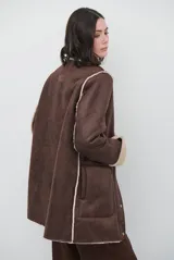Chaquetón de efecto cuero en color marrón, con interior y detalles en corderito color bordó. Presenta cierre frontal con cremallera y botones a presión, cuello solapa y mangas largas con puños de corderito.