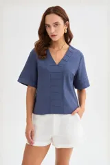 Blusa de viscosa color beige con cuello en V, mangas cortas amplias y detalles de pespuntes decorativos en el frente y las mangas.