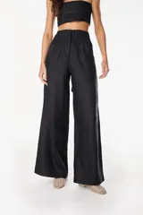 Pantalón de lino blanco de corte ancho y fluido, con cintura alta que incorpora una sobrepretina ancha desmontable con pliegues horizontales.