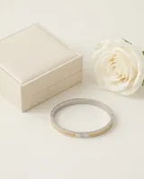 Esclava rígida de acero con baño de oro y detalle de circonia incrustada. Diseño minimalista con grabado.