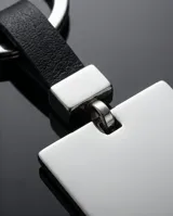Llavero de acero con placa cuadrada pulida y correa de cuero sintético negro. Incluye un sistema de sujeción metálico para llaves.