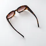 Lentes de sol con armazón carey y diseño envolvente, cuentan con filtro UV400 y patillas anchas con detalle ovalado metálico.